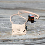 Nature's Mini Gift Kits, small white leather pouch with two 100% natural oils, on a log by the beach.