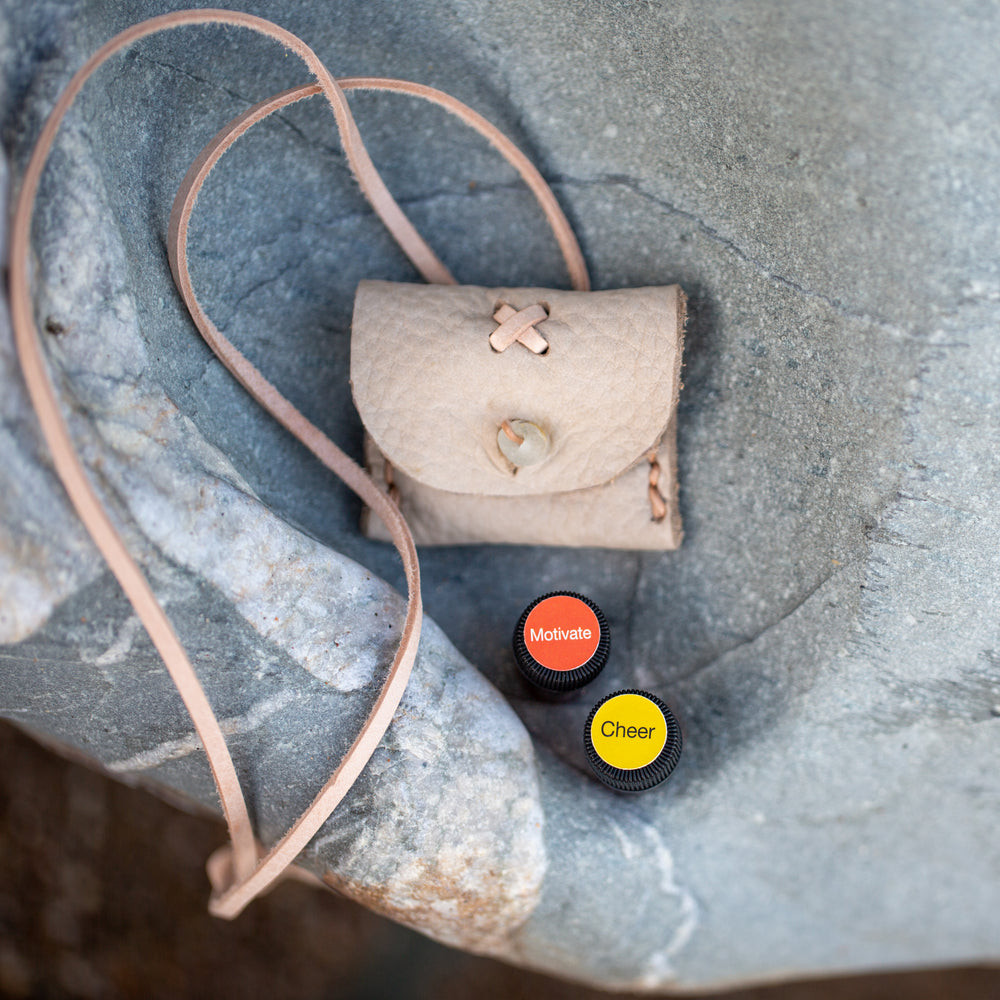 Small light leather pouch with 2 100% natural oils sitting on a rock by the sea.