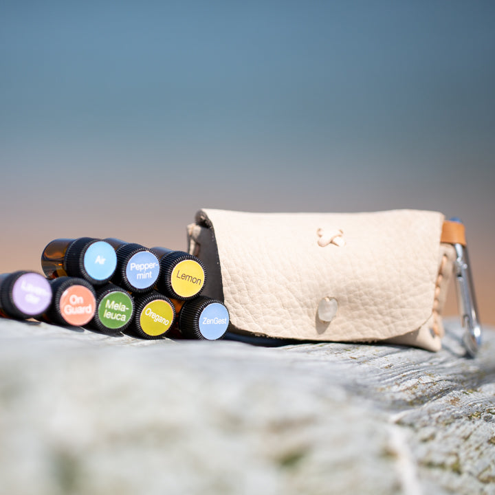 Nature's First Aid Kit, white leather pouch with eight 100% natural oils, on a log by the beach.
